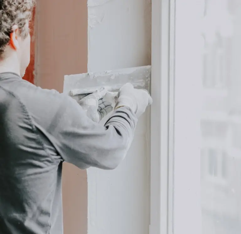 Handwerker verputzt Wand neben Fensterrahmen mit Spachtel. Renovierungsarbeiten, Trockenbau, Wandglättung.